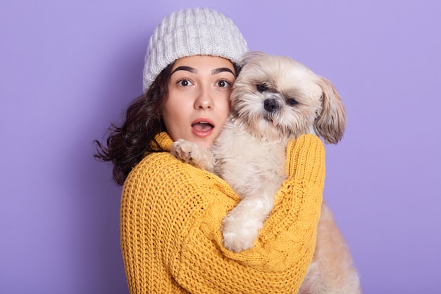 Shocked pretty girl holding dog and looking directly at camera with opened mouth