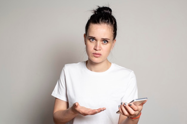 Shocked puzzled young woman holds a smartphone in her hand sees bad news