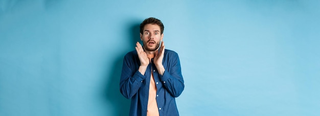 shocked and scared young man standing in stupor raising hands up and gasping speechless standing on