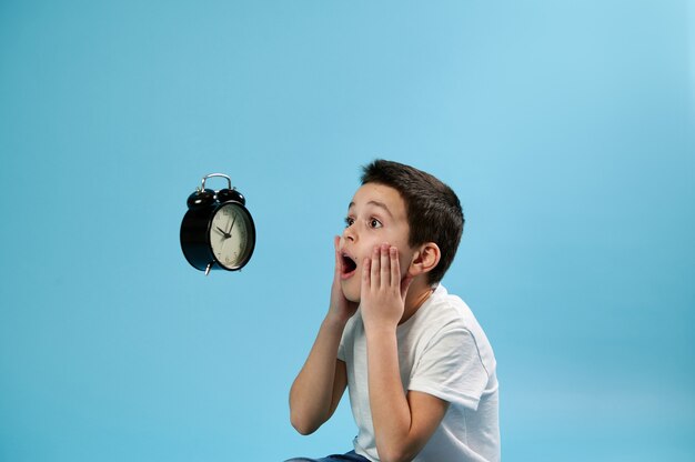 A shocked schoolboy looking with horror at a flying alarm clock and holding his face with his hands