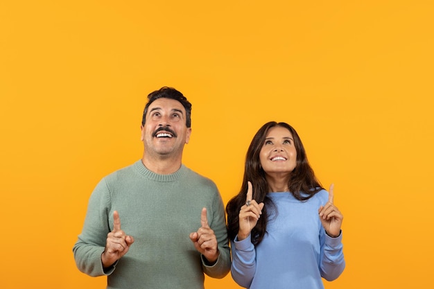 Shocked senior caucasian couple in casual point finger up at copy space