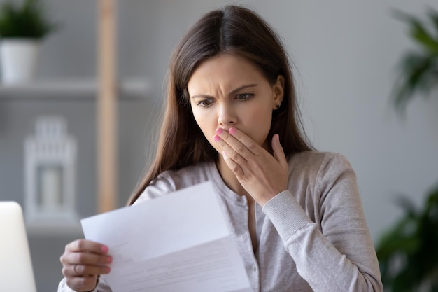 shocked stressed young woman reading document letter from bank about loan debt financial problem frustrated worried about bills notification troubled with bad news or failed test results in mail