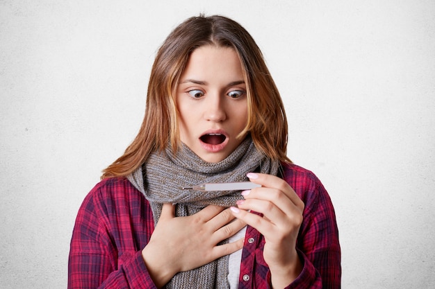 Shocked stupefied female stares at thermometer,