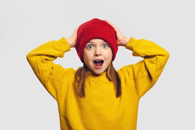 Shocked stupefied little kid looks with widely opened mouth keeps hands on