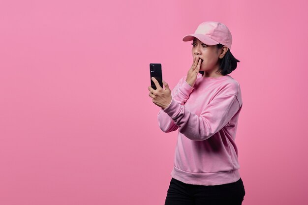 Shocked and surprised Asian woman wearing pink jacket when receiving incoming message on smartphone