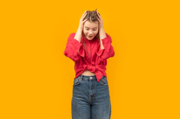 Shocked and surprised girl holds head with hands and looks down Portrait of teenage girl on yellow background