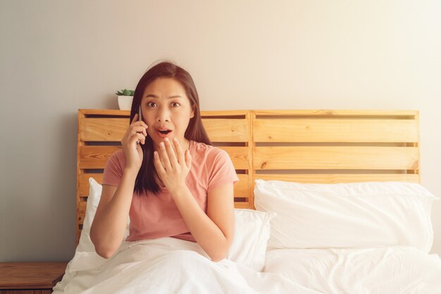 Shocked and surprised woman is having a phone conversation on her bed.