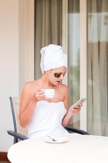 Shocked or surprised woman in undereye patches reading message and drinking coffee at hotel terrace resort morning holiday concept bad news