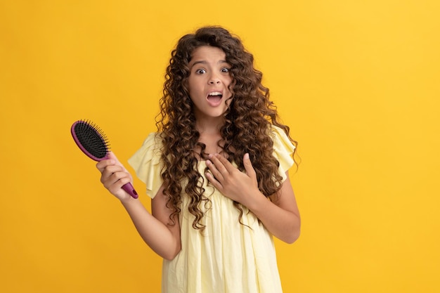 Shocked teen girl with long curly hair holding comb hairbrush for combing, daily habits.