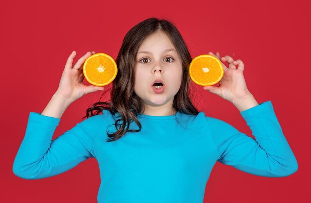 Shocked teen kid holding orange fruit on purple background