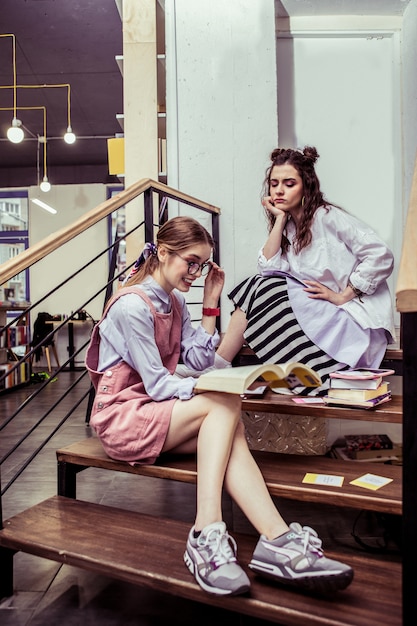 Shocked with content. busy good-looking girls spending time on
wooden stairs in co-working area and reading materials