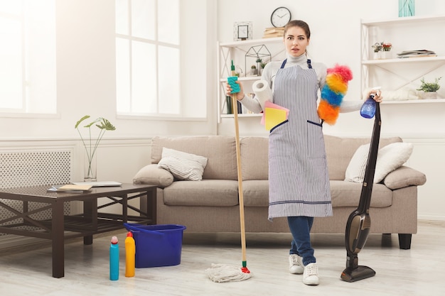 Shocked woman cleaning house with lots of tools