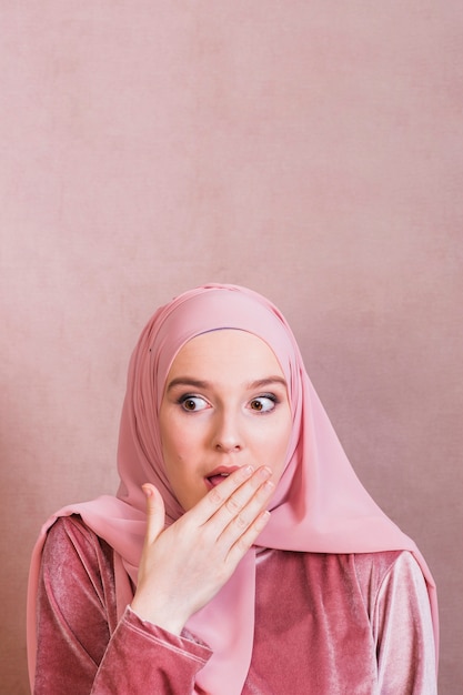 Photo shocked woman covering lips with palm against colored background