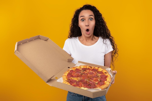 Shocked woman holding box with pizza at studio