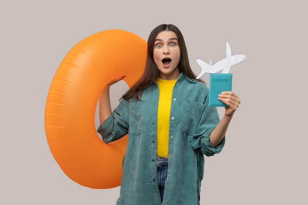 Shocked woman holding orange rubber ring passport document and paper airplane traveling abroad