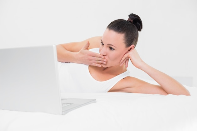 Shocked woman looking at laptop in bed