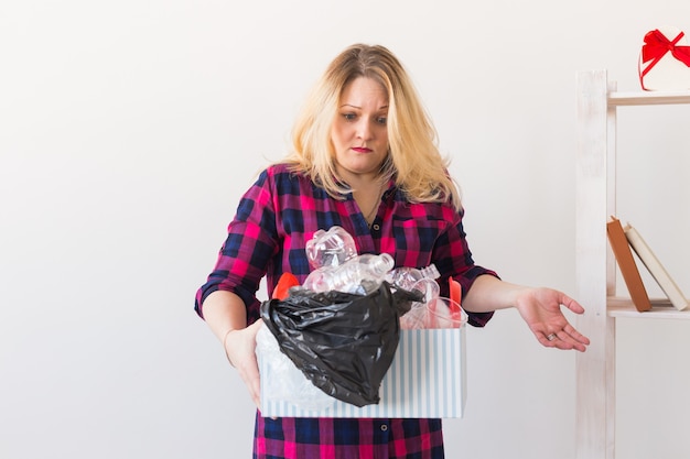 Photo shocked woman looks with opened eyes and worried expression, holding box with various plastic wastes