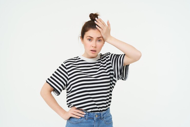 Photo shocked woman slaps her forehead holds hand on head and looks startled concerned re something bad