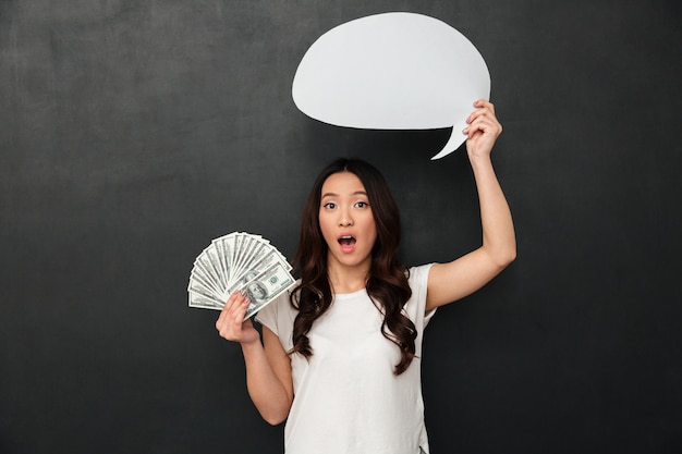 Photo shocked woman in t-shirt holding money and blank speech bubble