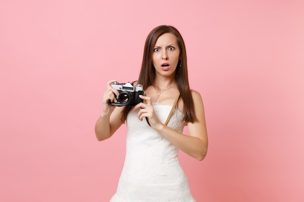 Shocked woman in white dress holding retro vintage photo camera, choosing staff, photographer 