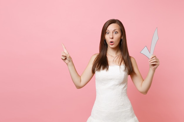 Shocked woman in white dress pointing index finger aside holding check mark