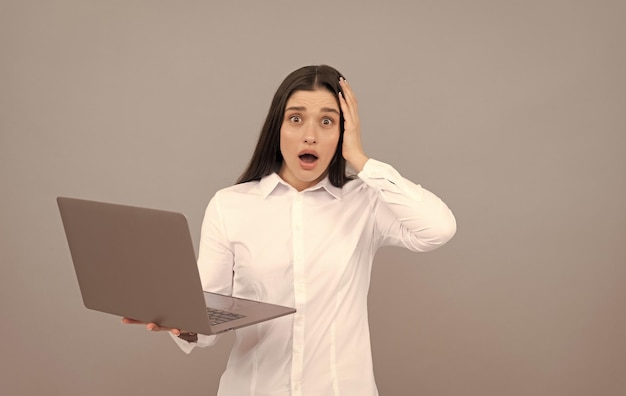 La donna scioccata in camicia bianca tiene il computer ha molto lavoro superlavoro