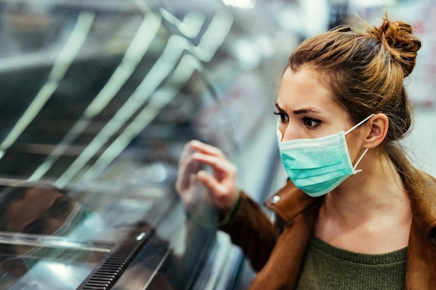 Shocked woman with face mask looking at empty shelves while buying in the supermarket during virus pandemic