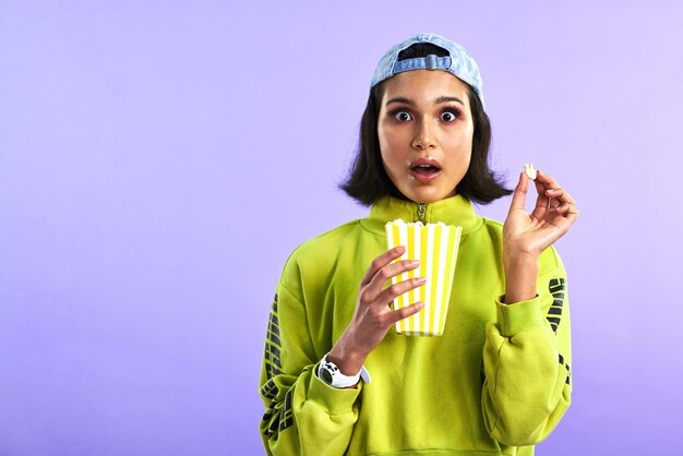 Shocked wow and woman with popcorn for a movie or streaming service or cinema and in studio against a purple background video entertainment and film or television or omg and box snack on mock up