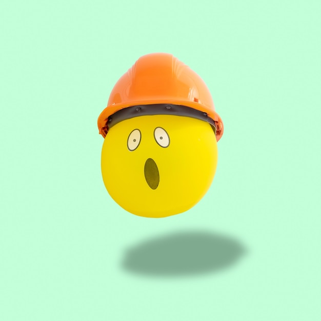 Shocked yellow balloon face with construction mask floating on pastel green background