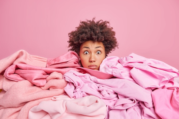 Shocked young African American woman sticks head through pile of laundry stares stunned at camera