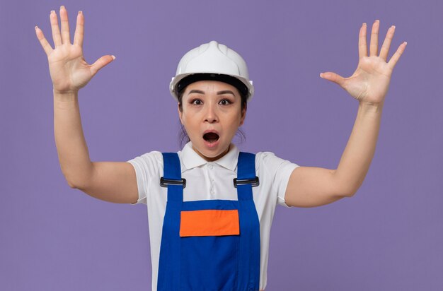 Photo shocked young asian builder woman with white safety helmet standing with raised hands