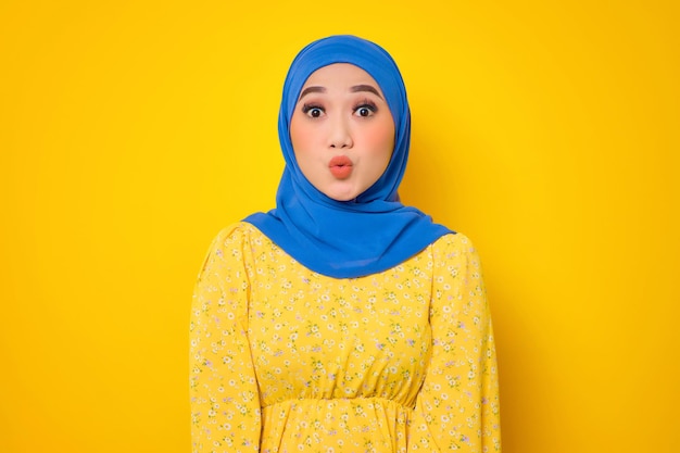 Shocked young asian woman in casual dress looking at camera\
with stunned face isolated on yellow background