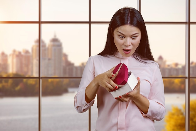 Shocked young asian woman is opening heart shape gift box
