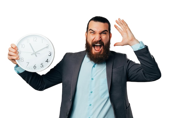 Photo shocked young bearded man screams load while holding a round white clock