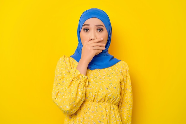 Shocked young beautiful Asian Muslim woman covering her mouth with hands isolated over yellow background
