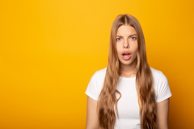 口を開けて黄色に分離されたショックを受けた若いブロンドの女の子