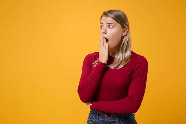 Shocked young blonde woman girl in casual clothes posing isolated on yellow orange background studio portrait. people lifestyle concept. mock up copy space. looking aside, covering mouth with hand