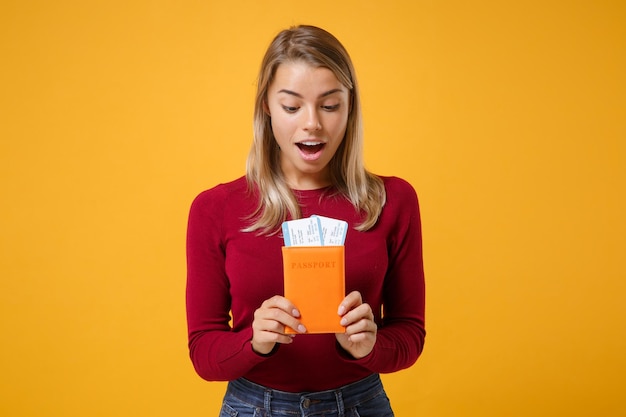 Shocked young blonde woman girl in casual clothes posing isolated on yellow orange wall background studio portrait. people lifestyle concept. mock up copy space. hold passport boarding pass tickets
