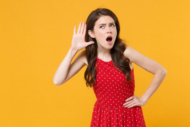 Shocked young brunette woman girl in red summer dress posing isolated on yellow background studio po