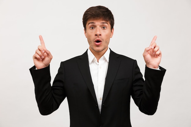 Shocked young businessman standing isolated on white wall.