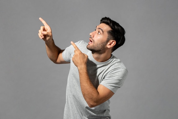 Shocked young Caucasian man gasping with hands pointing up isolated light gray studio background
