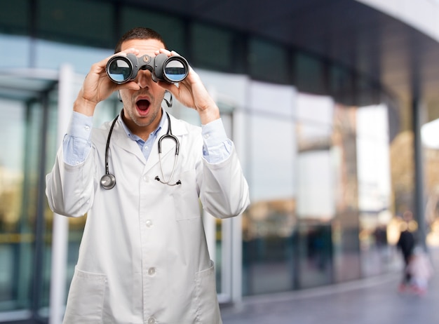 Photo shocked young doctor using a binoculars