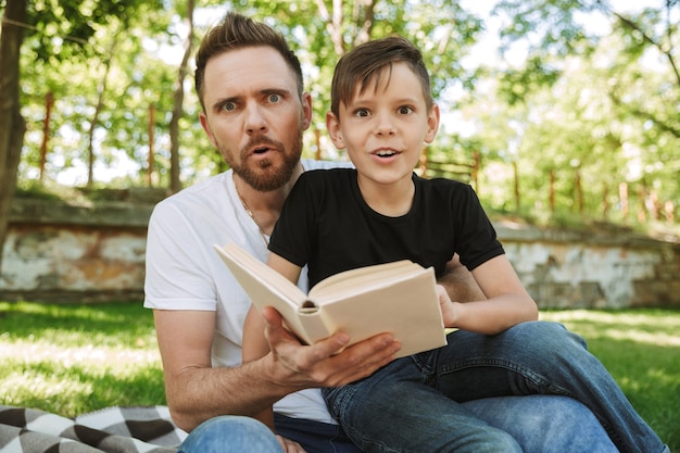 Shocked young father sitting with his little son reading book.