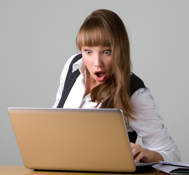 Shocked young girl is looking at a laptop reading messages in social networks