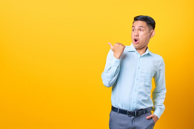 Shocked young handsome businessman pointing finger away at copy space on yellow background