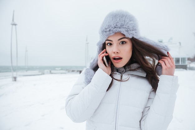 彼女の電話で話している帽子をかぶってショックを受けた若い女性。