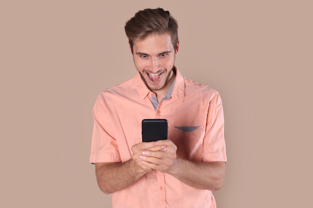 Photo shocked young man standing isolated over beige background, using mobile phone