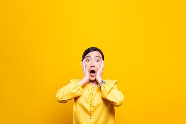 Shocked young woman against yellow background