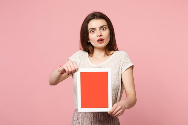 Shocked young woman in casual light clothes posing isolated on pastel pink background studio portrait. People lifestyle concept. Mock up copy space. Holding tablet pc computer with blank empty screen.