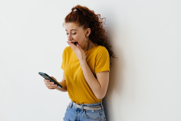 Shocked young woman using cell phone Excited young woman using mobile phone isolated on white background Technology and emotion concept